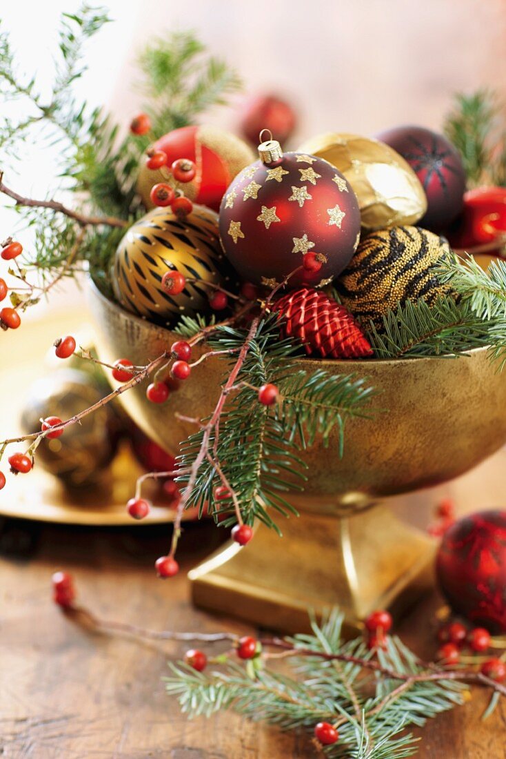 Weihnachtskugeln auf Tannen- und Beerenzweigen in vergoldeter Schale