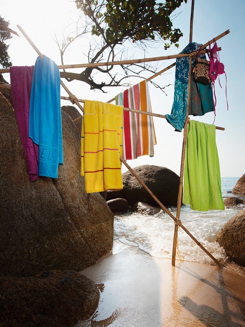 Beach towels hanging on construction of poles amongst boulders on beach