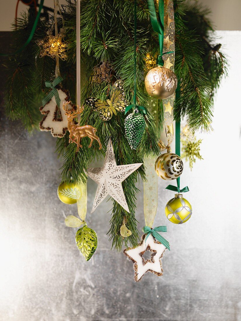 Tannenzweig mit Weihnachtsdeko vor silberfarbener Wand aufgehängt