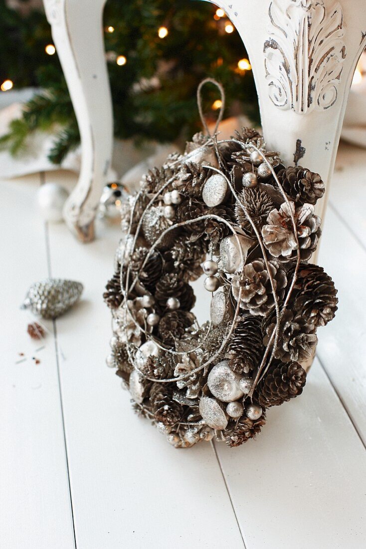 Wreath of pine cones and Christmas decorations leaning on chair leg on white wooden floor