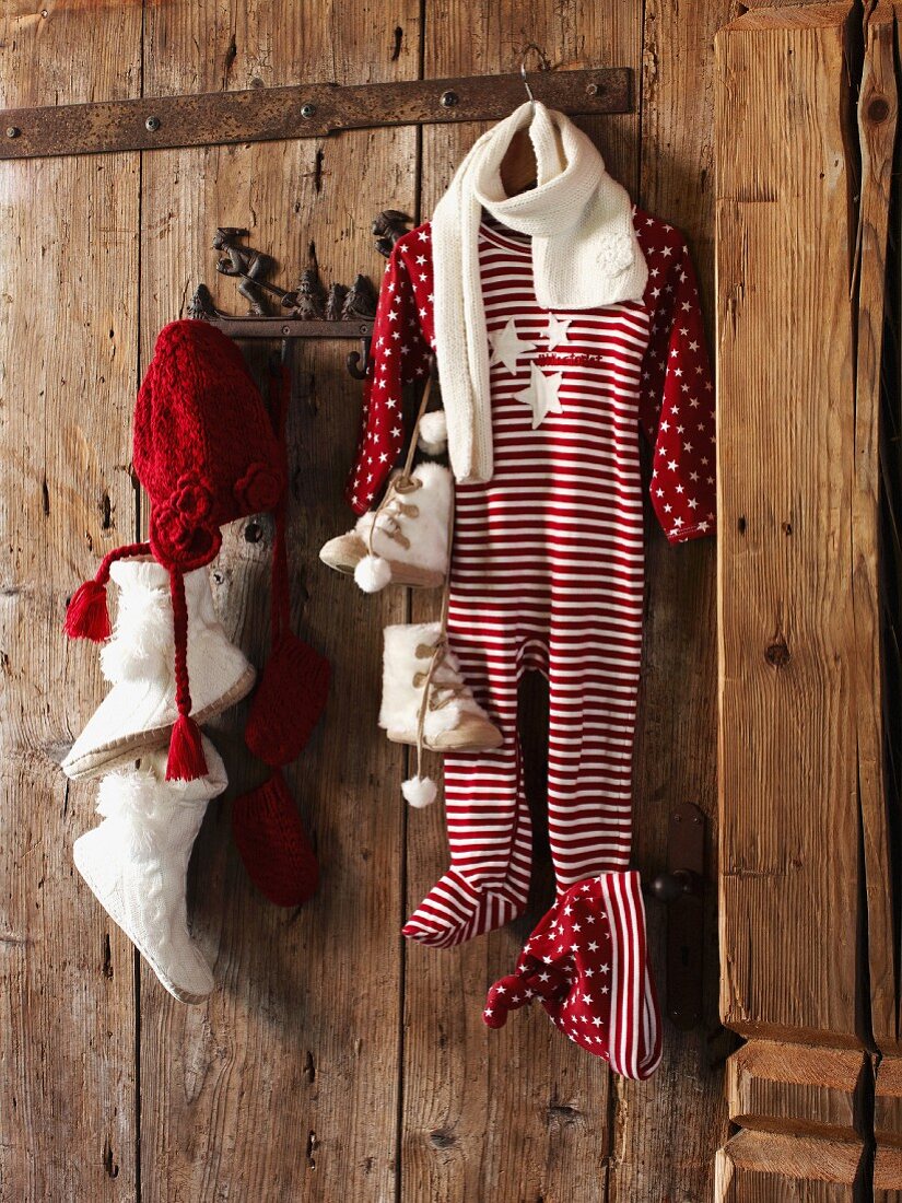 Baby clothes with festive motifs hanging from pegs on rustic wooden wall