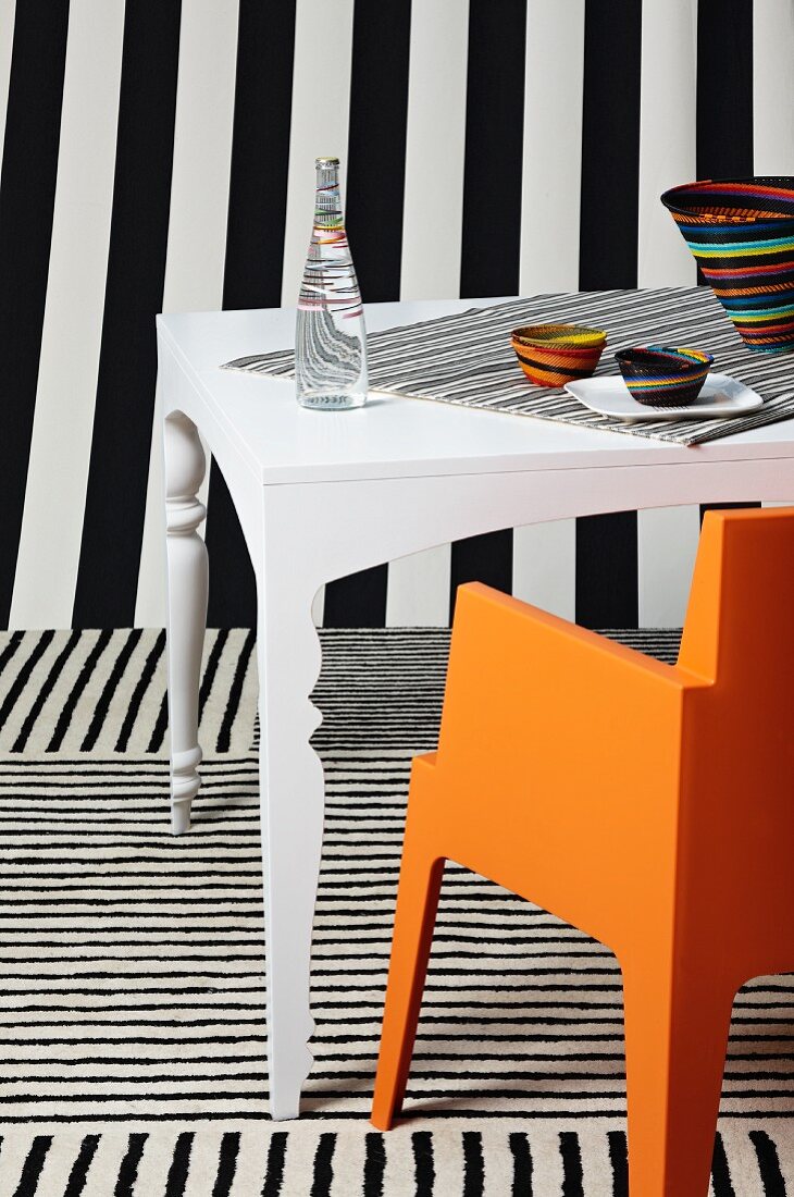 Weisser Tisch mit orangefarbenem Stuhl inmitten schwarz-weisser Streifenvariationen