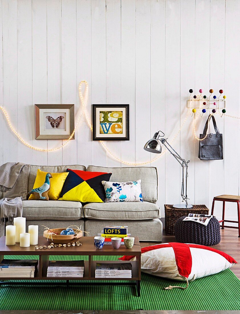Candles on coffee table and sofa in front of fairy lights on white wooden wall