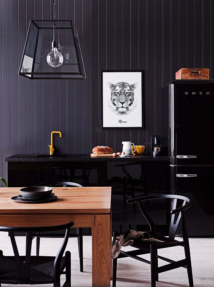 Klassikerstühle an Holztisch vor schwarzer Küchenzeile an schwarzer Holzwand