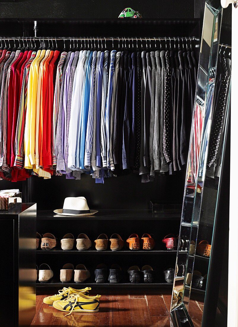 Nach Farben sortierte Hemden und Schuhe in schwarz getöntem, begehbarem Kleiderschrank