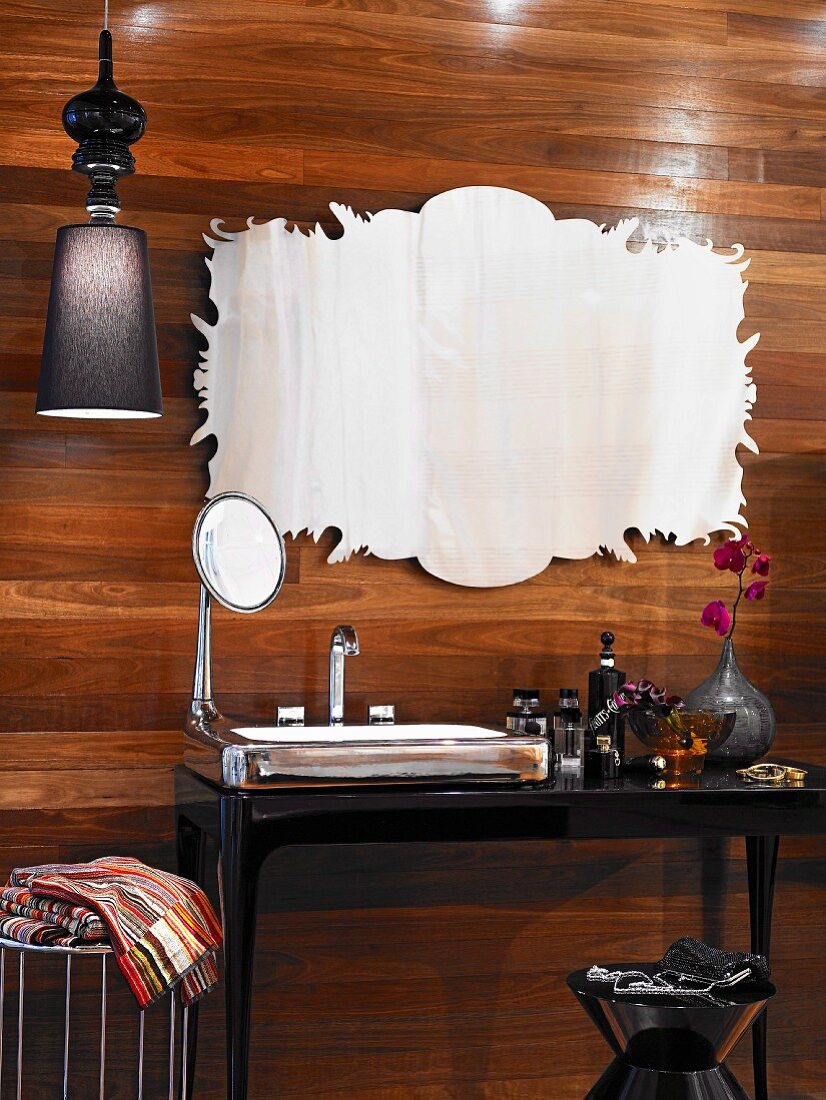 Eleganter schwarzer Waschtisch mit Kunstwerk an edler Holzverkleidung, verschiedene Flacons und silberfarbener Spiegel