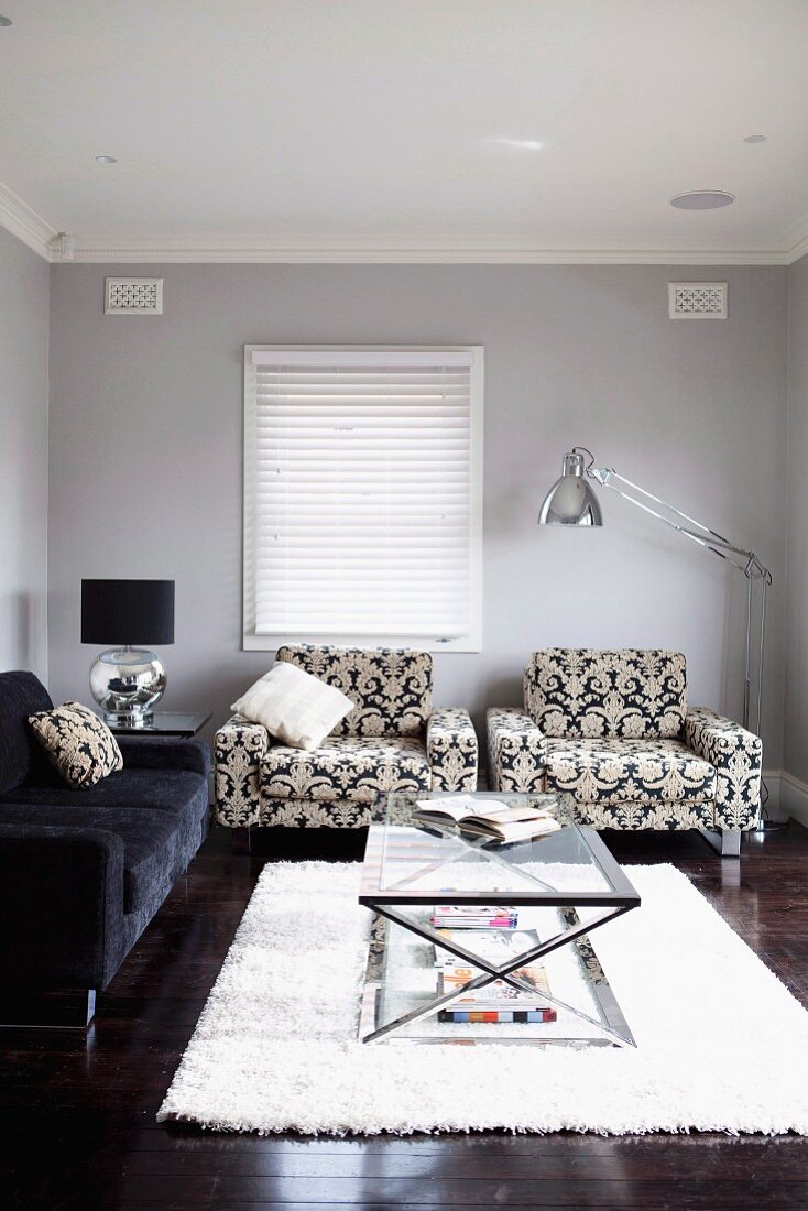 Glastisch mit Metallgestell auf hellem Flokatiteppich vor gemusterten Sesseln und Sofa in traditionellem Wohnzimmer mit hellgrau getönten Wänden