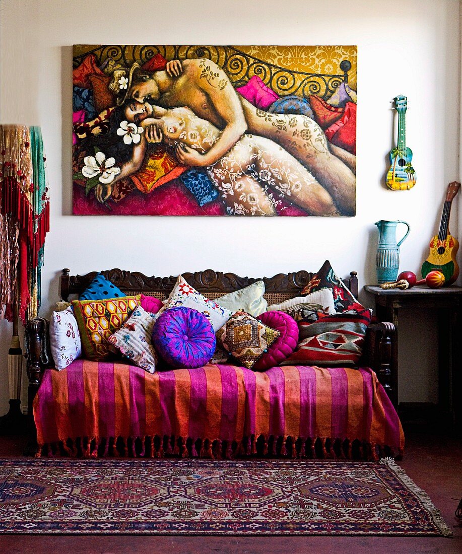 Antique sofa with colourful collection of blankets and cushions below painting of couple embracing