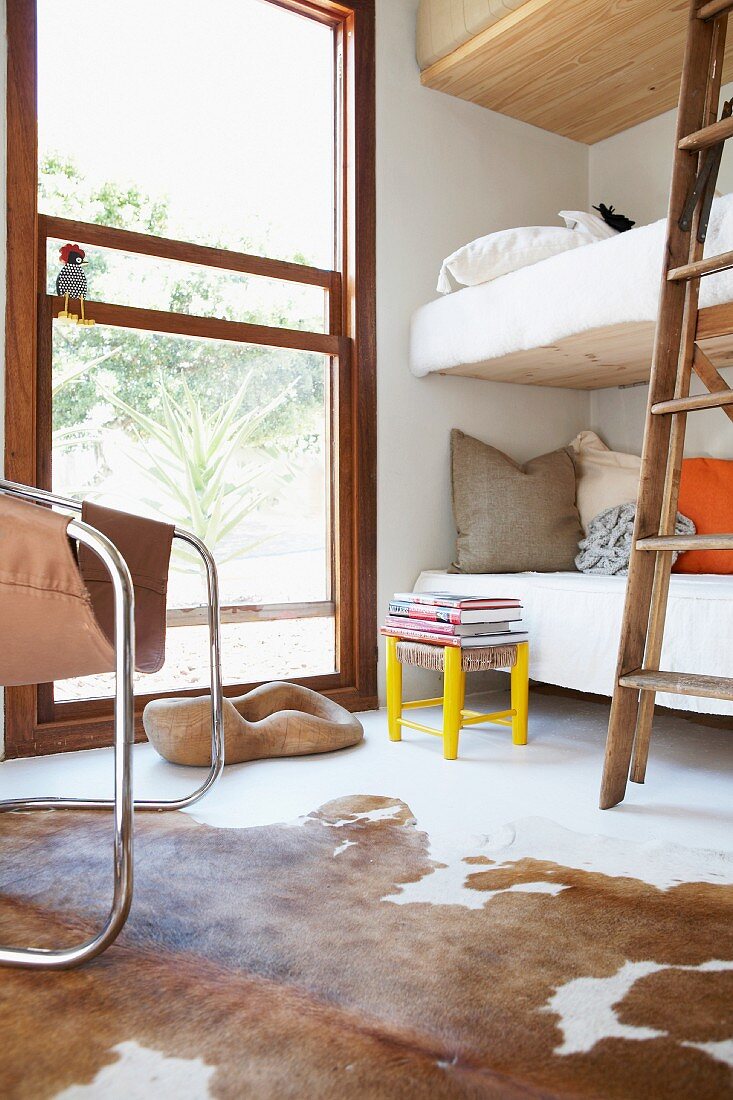 Bunk beds next to floor-to-ceiling window with view of garden and cowhide rug on floor in foreground
