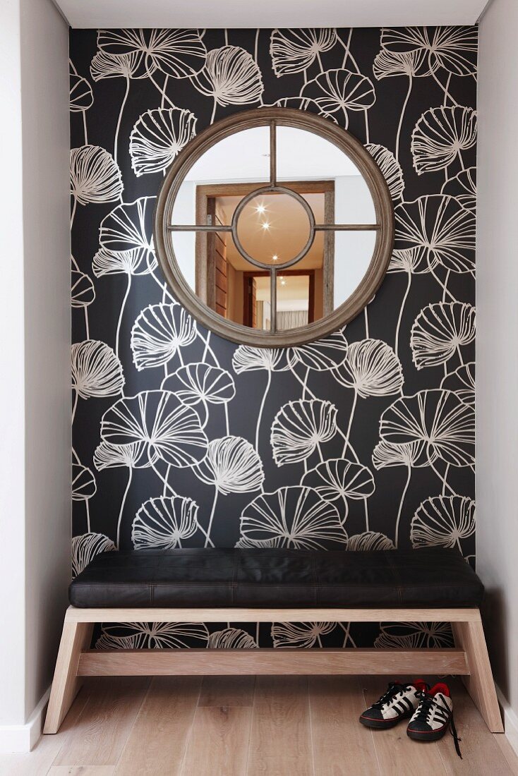 Round, latticed window on floral wallpaper and bench with black leather seat cushion in niche