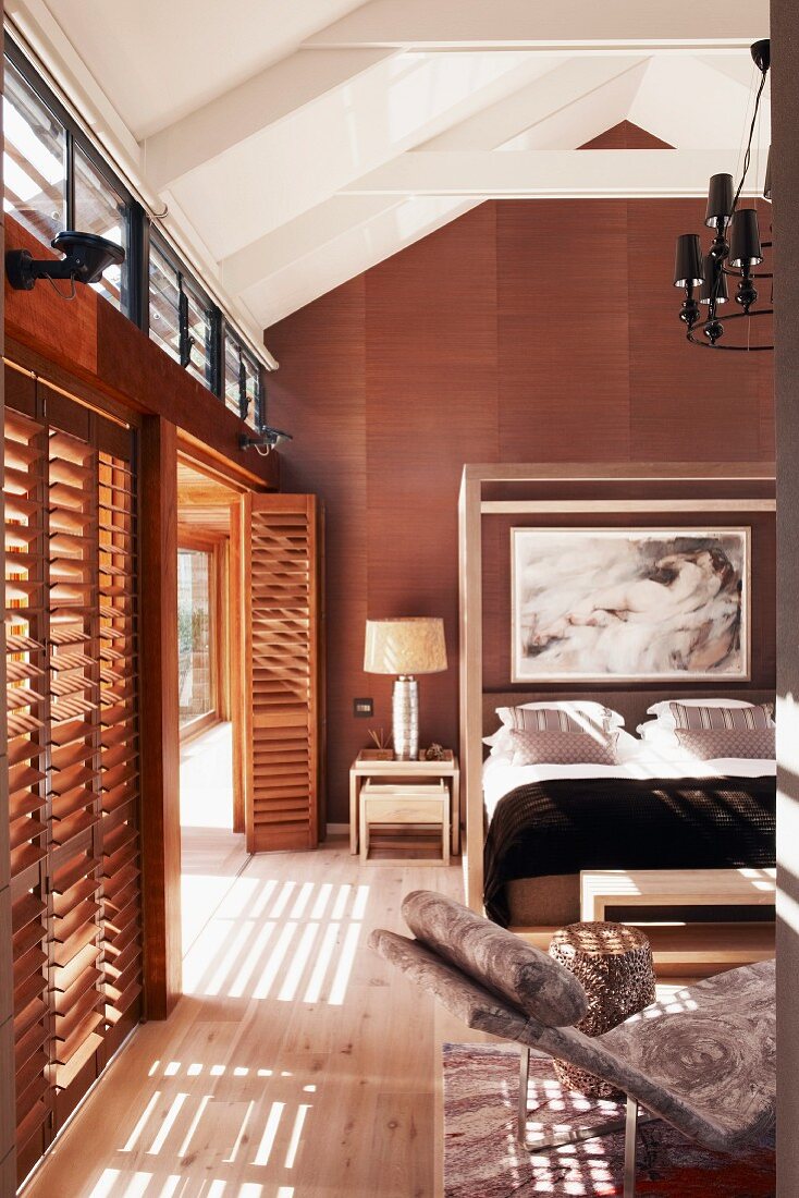 Elegant bedroom in light and dark natural shades; glass wall on one side with slatted shutters