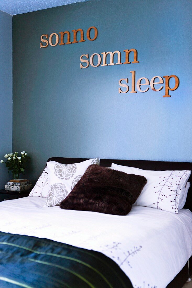 The word 'sleep' written in three languages decorating wall painted slate blue above double bed