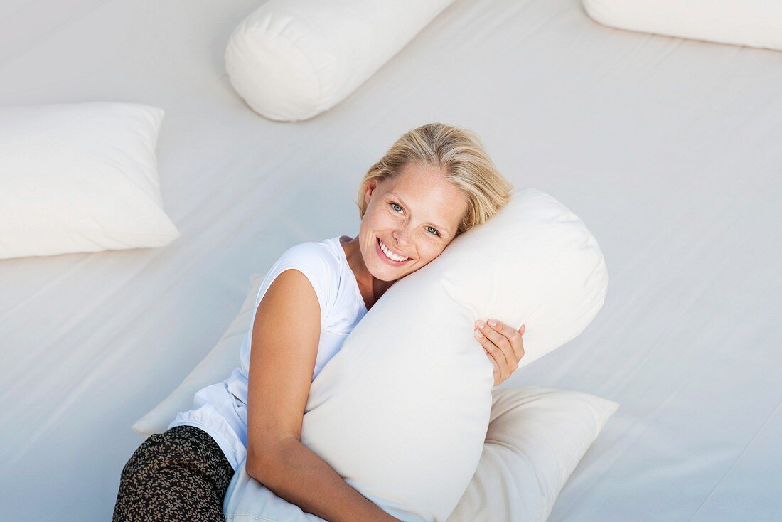 Junge Frau umarmt Kissen auf dem Bett