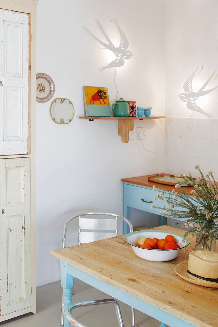 Küchentisch mit hellblauem Gestell vor Vintage Küchenzeile in Zimmerecke unter Wandleuchten mit Vogelmotiv