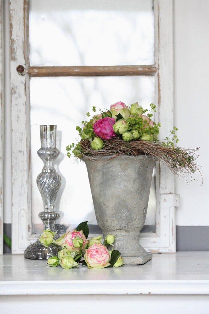 Arrangement of roses with stone and glass vases in front of old window casement