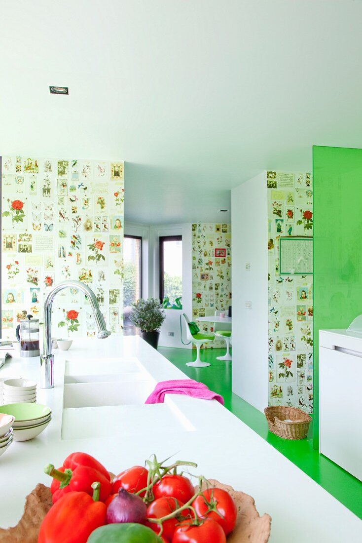 Schale mit frischem Gemüse auf Arbeitsplatte aus weißem Mineralwerkstoff und integrierter Spüle in moderner, offener Küche mit grünem Fußboden