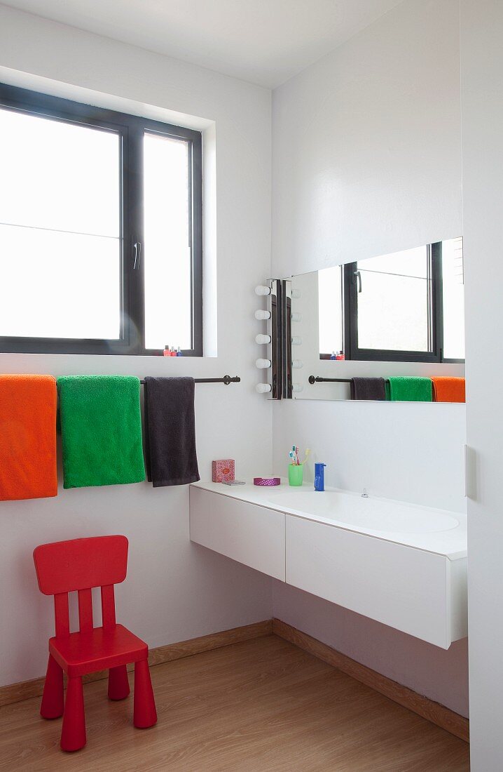 Red child's chair below towels on rack and modern sink in bathroom