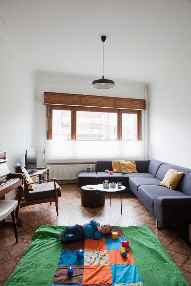 Narrow interior with sofa combination and baby playing with toy cups on play mat