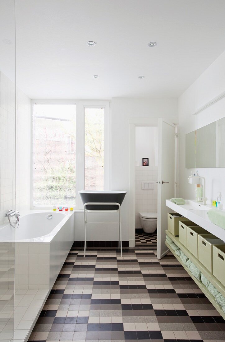 Modern bathroom in period building with grey tiled floor, washstand with storage boxes and baby bath on metal frame