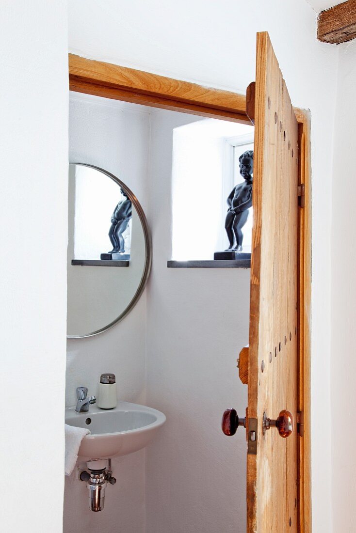 View through open wooden door into bathroom with sink below round mirror