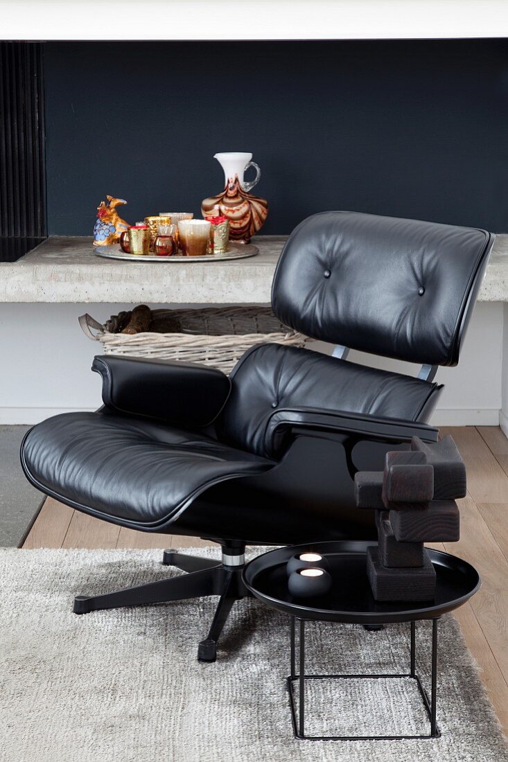 Charles Eames lounge chair with black leather cover and side table in front of concrete shelf