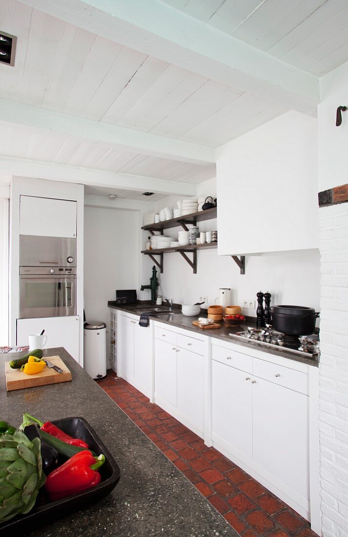 Küchenzeile mit weissen Fronten und Mittelblock mit Steinarbeitsfläche in ländlichem Ambiente