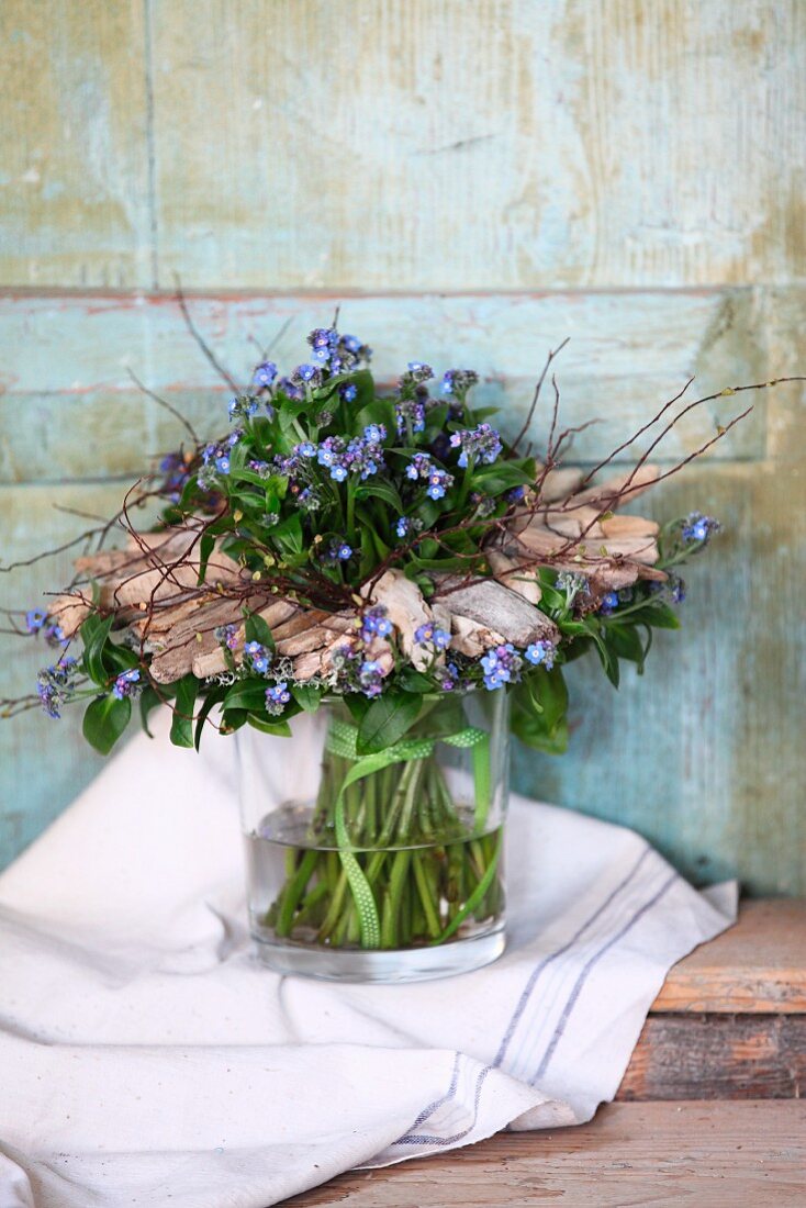 Posy of forget-me-nots in glass jar with wreath of driftwood fragments
