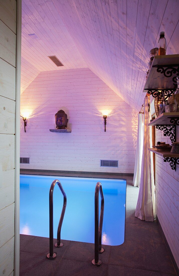 Swimming pool with atmospheric lighting, wood-clad walls and head of the Buddha on shelf as focal decorative element