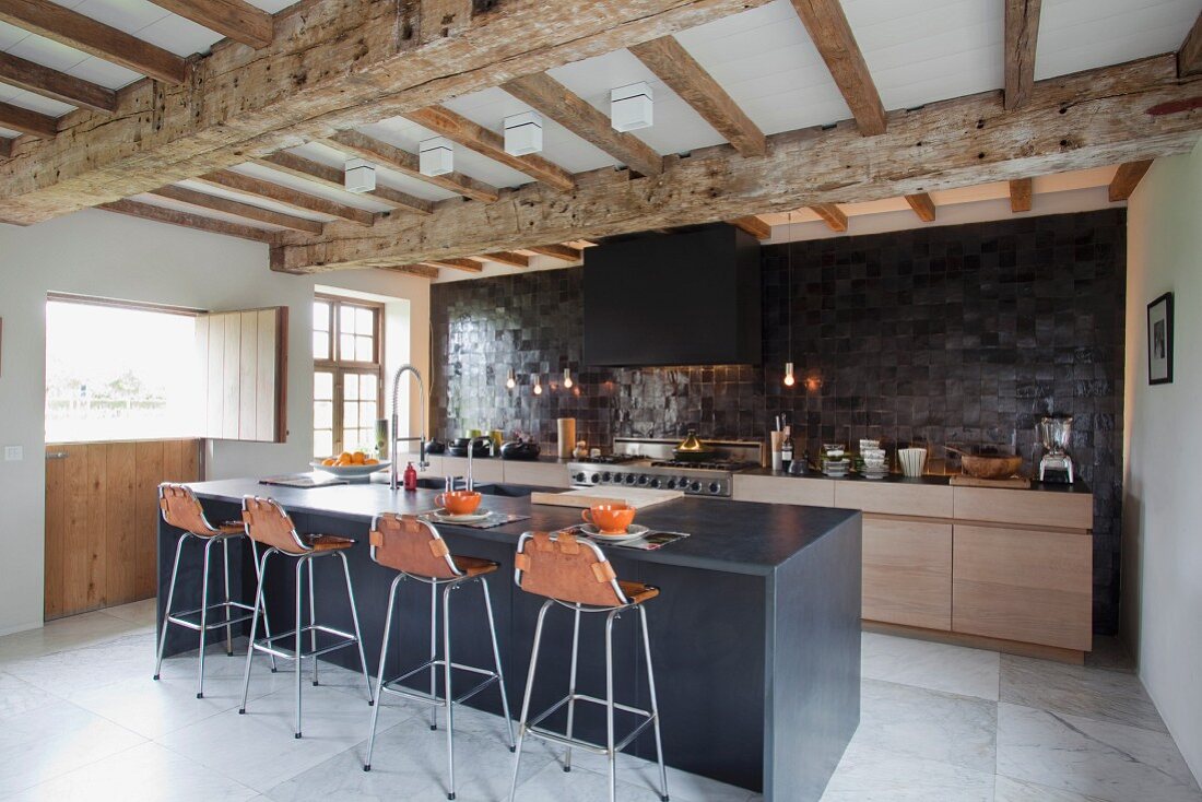 Spacious, modern kitchen with breakfast bar below renovated wood-beamed ceiling in converted stable