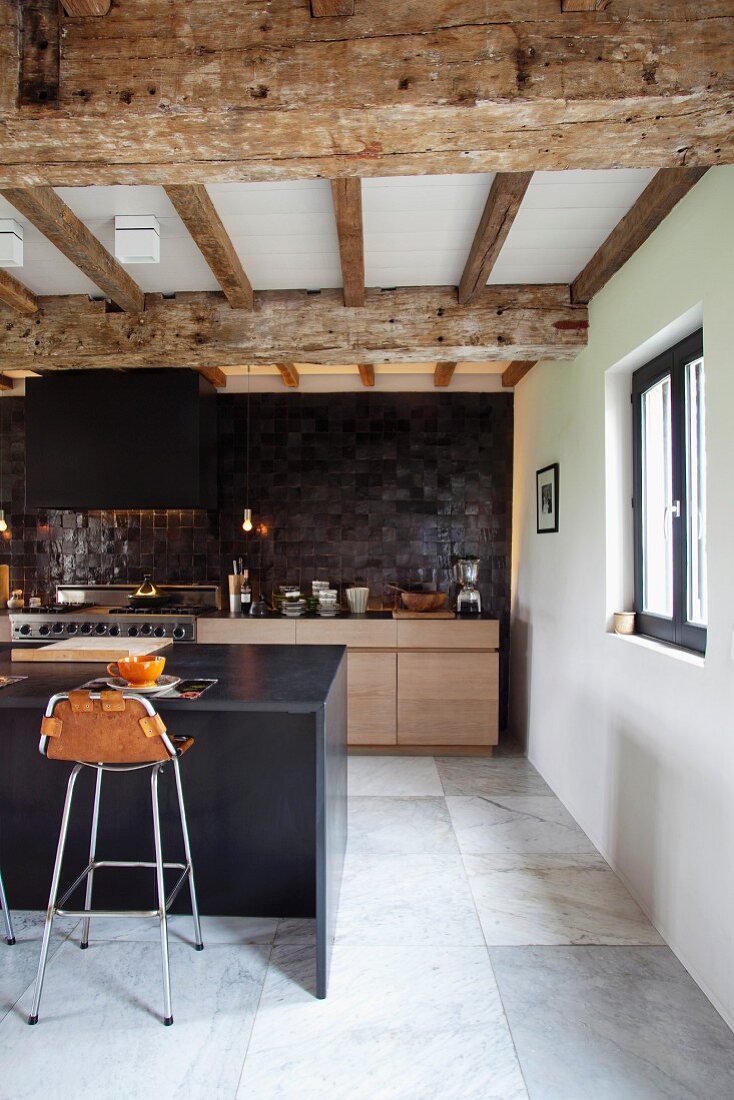 Modern designer kitchen with bar stools at breakfast bar below renovated wood-beamed ceiling in converted stable