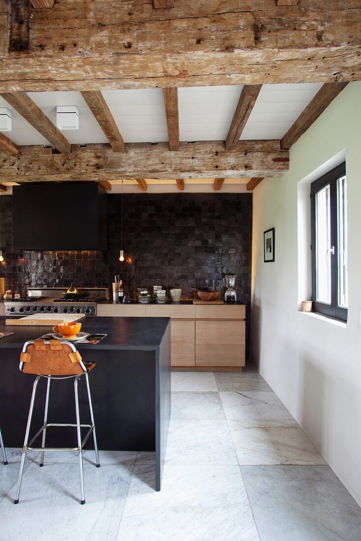 Moderne Designerküche mit Barhocker an Frühstückstheke unter der renovierten Holzbalkendecke in ehemaligem Stall