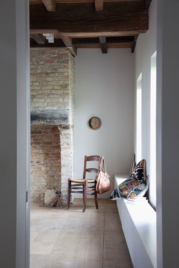 Blick durch offene Tür auf Holzstuhl neben altem, offenem Ziegelkamin