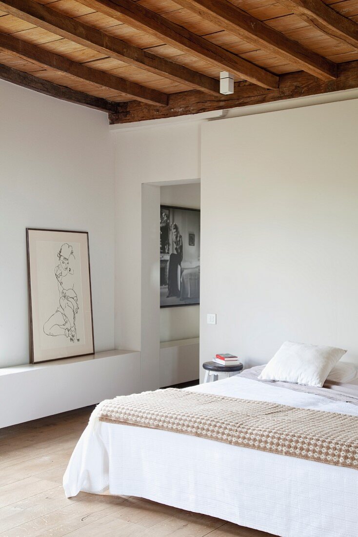 Double bed with simple wooden stool as bedside table and nude artwork next to open doorway leading to adjacent room