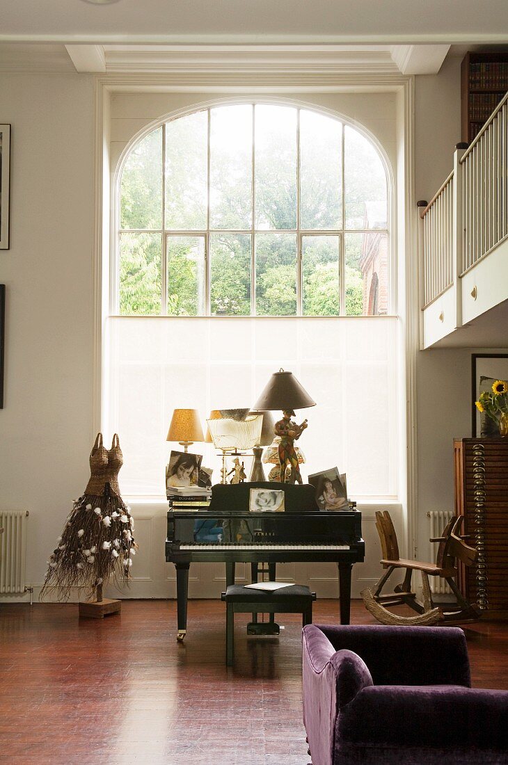 Grand piano and antique rocking horse in front of tall, arched window in grand interior