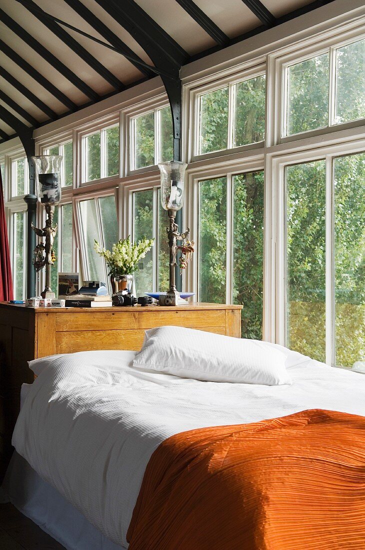 Bed with orange bedspread against glass wall