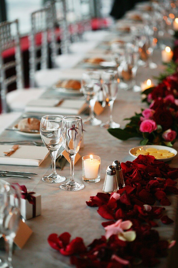 Hochzeitstafel mit Windlichtern und roten Rosenblütenblättern