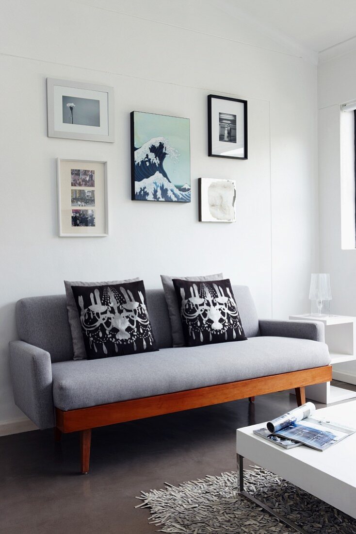Fotogalerie über grauem Sofa im Retrostil, weisser Couchtisch mit verchromten Füssen auf Hochflorteppich