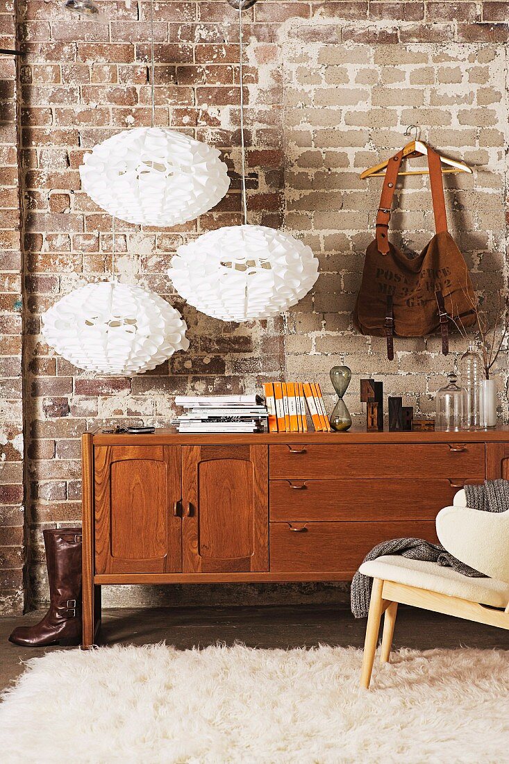 Vintage bag hanging from wooden coat hanger and three, white, designer pendant lamps decorating old brick wall