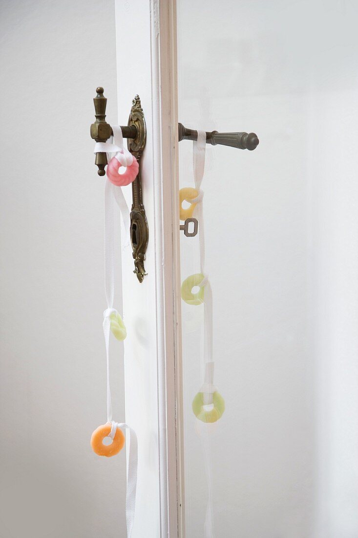 Dekobänder mit bunten, süßen Ringen auf Vintage Türdrückerpaar an Tür mit Glasfüllung