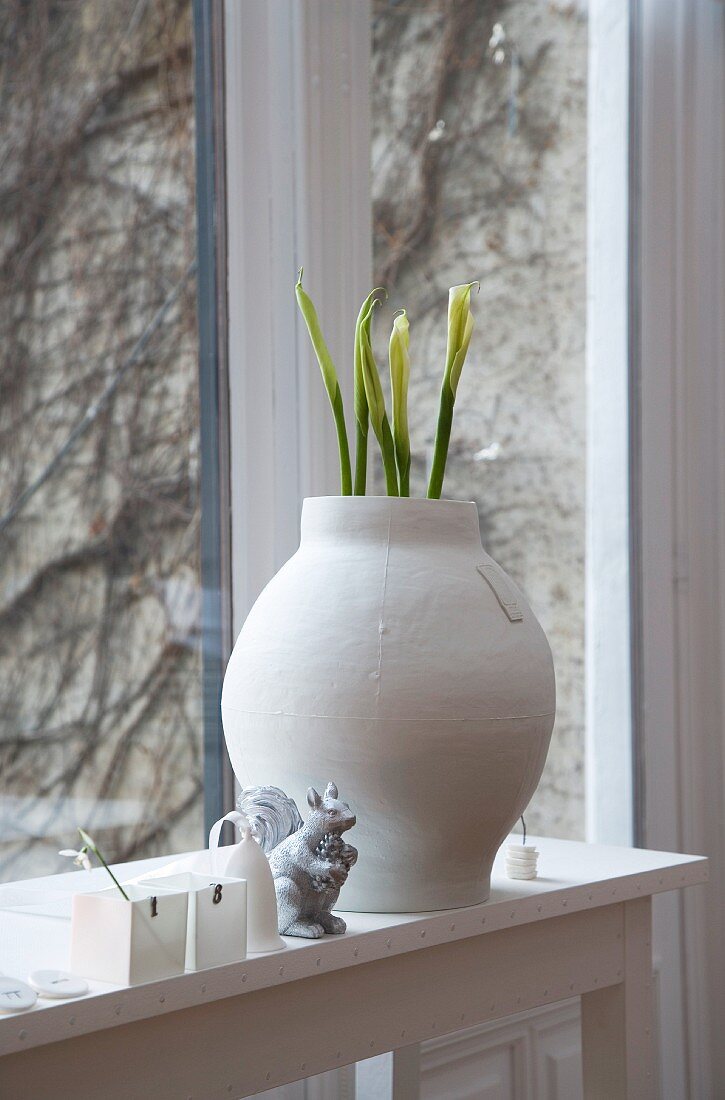 Flower buds in white clay pot on windowsill and view of climber-covered exterior wall