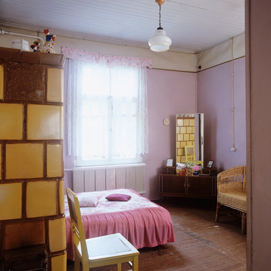 Double bed with pink counterpane opposite dressing table with tall mirror in pink-painted bedroom