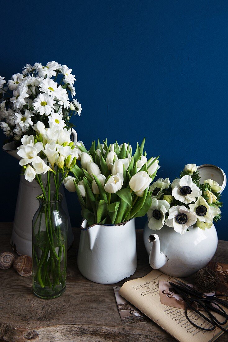 weiße Blütenpracht in Vintage-Behältern vor blauer Wand