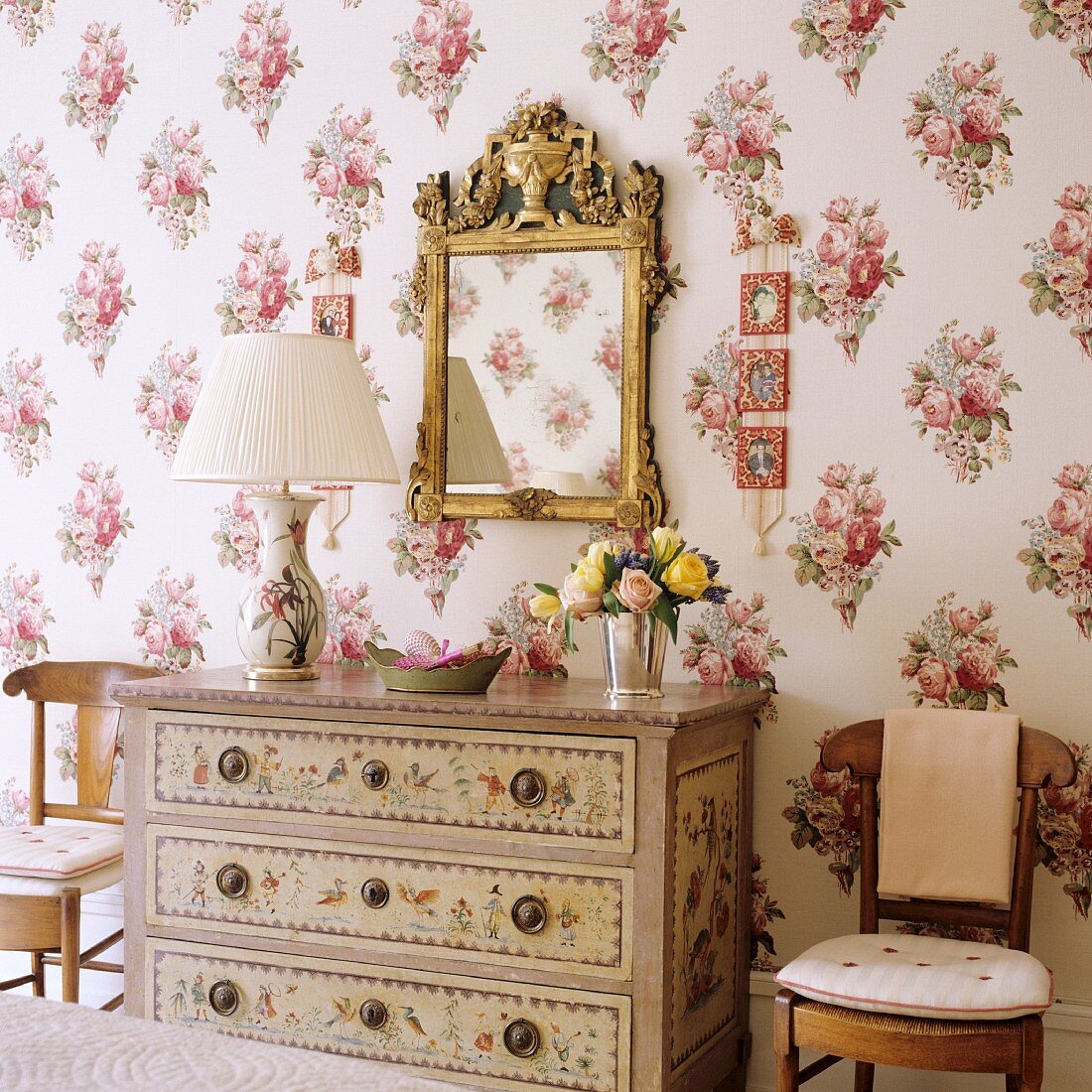 Tischleuchte mit Plisseestoffschirm auf bemalter Kommode vor Spiegel mit Goldrahmen an Wand mit Blumenmustern