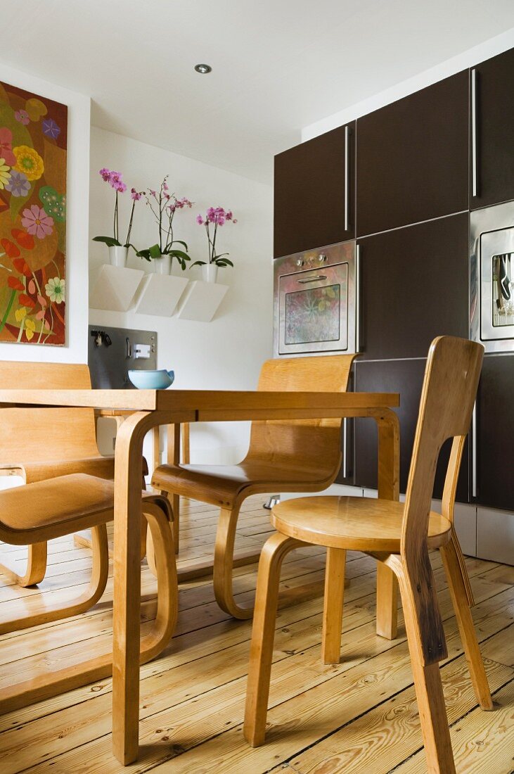 Dining area with Scandinavian-style wooden chairs and table in front of dark, modern, fitted kitchen cabinets