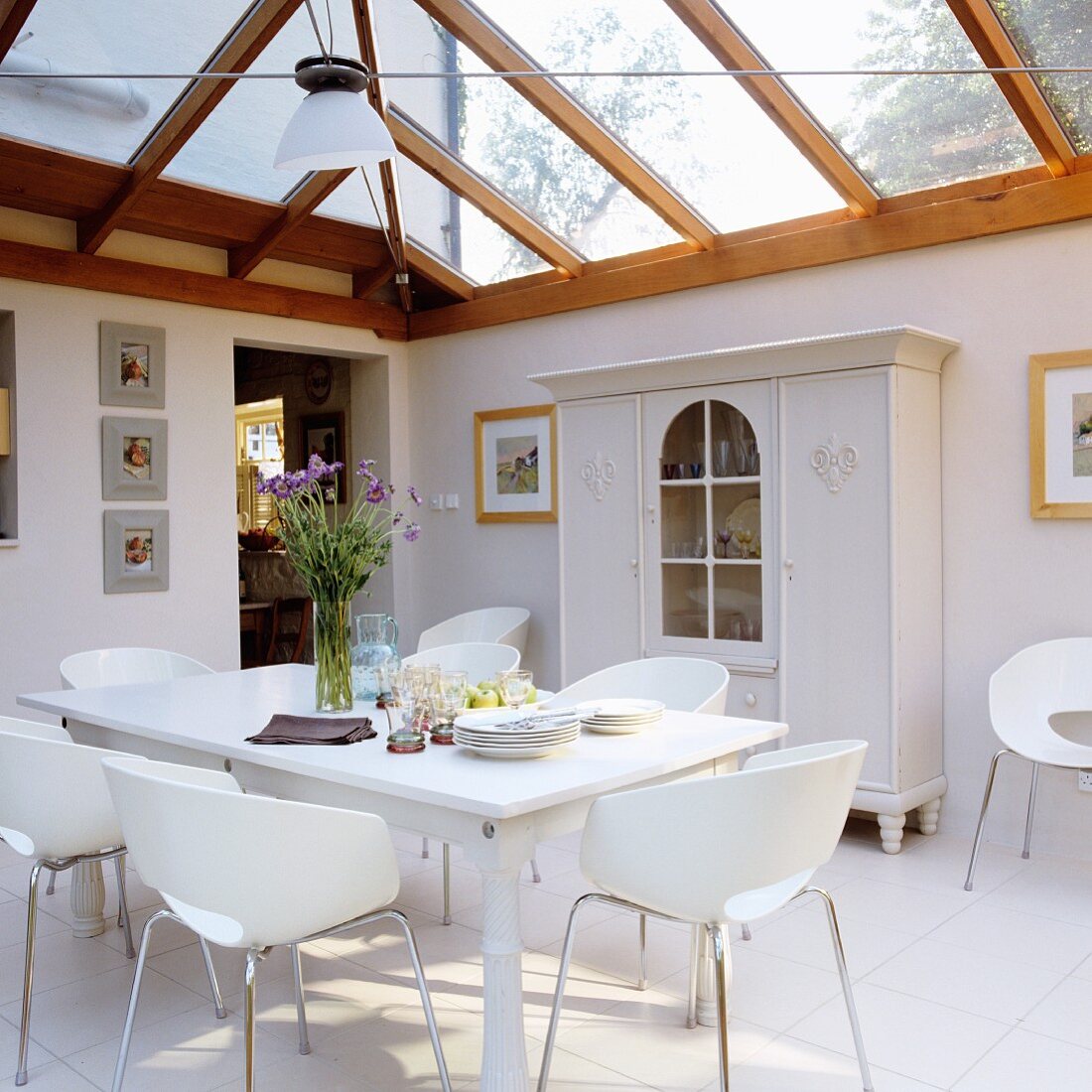 Modern, white shell chairs at dining table in front of farmhouse cupboard in extension with wood and glass roof structure