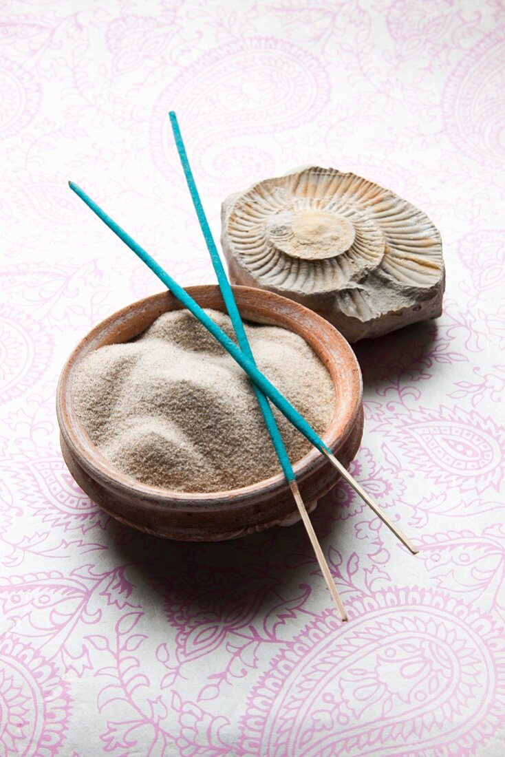 Feiner Sand in Keramikschale, Räucherstäbchen und eine Fossilie