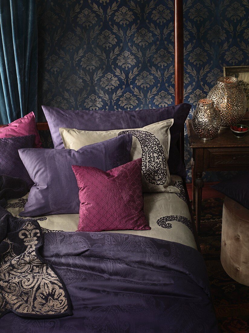 Schlafzimmer im Boheme-Look: Bett mit Dekokissen vor Wand mit gemusterter Tapete