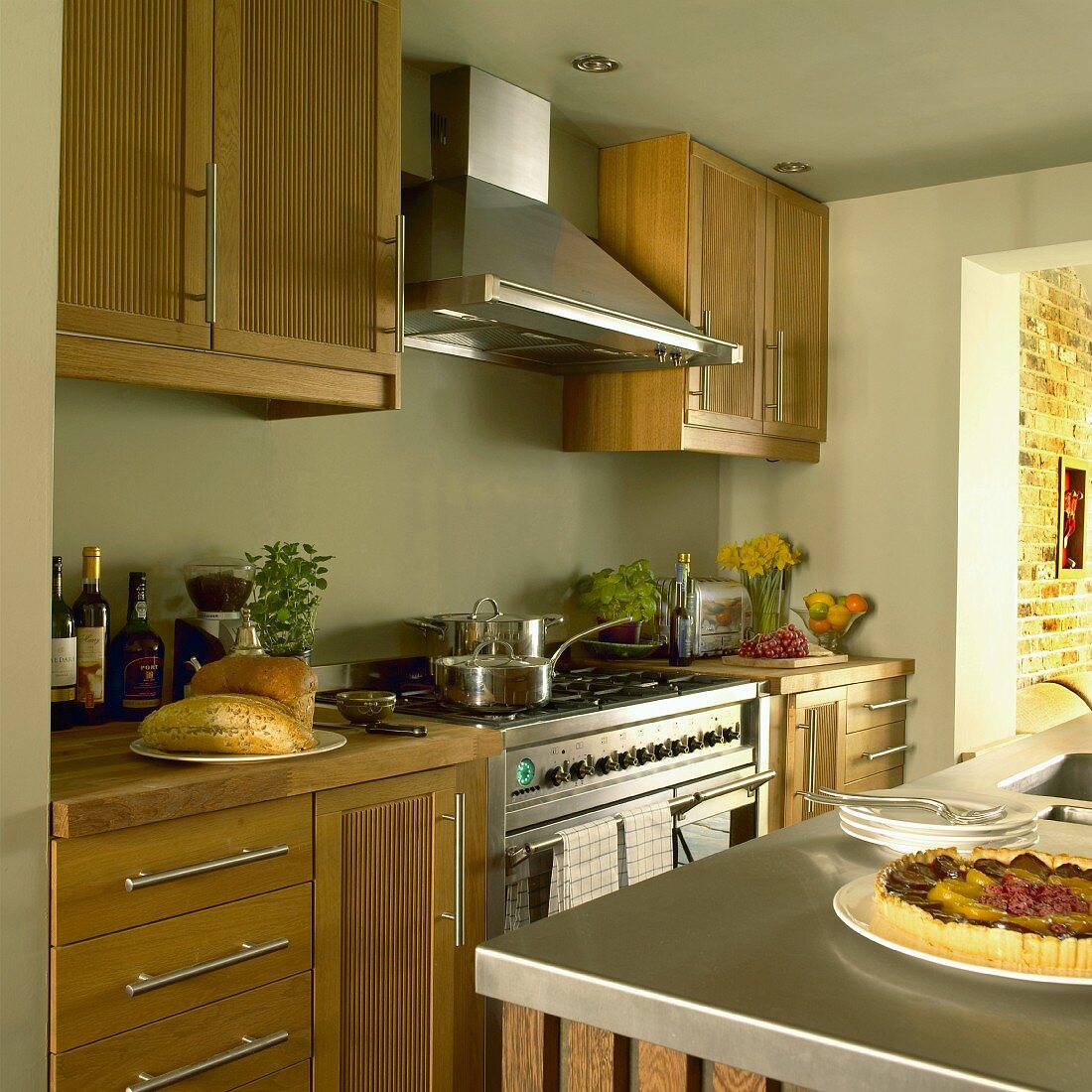 Küche im Landhausstil mit pastellgrünen Wänden, Holzmöbeln, Dunstabzugshaube über dem Herd und Mittelblock mit Spülbecken
