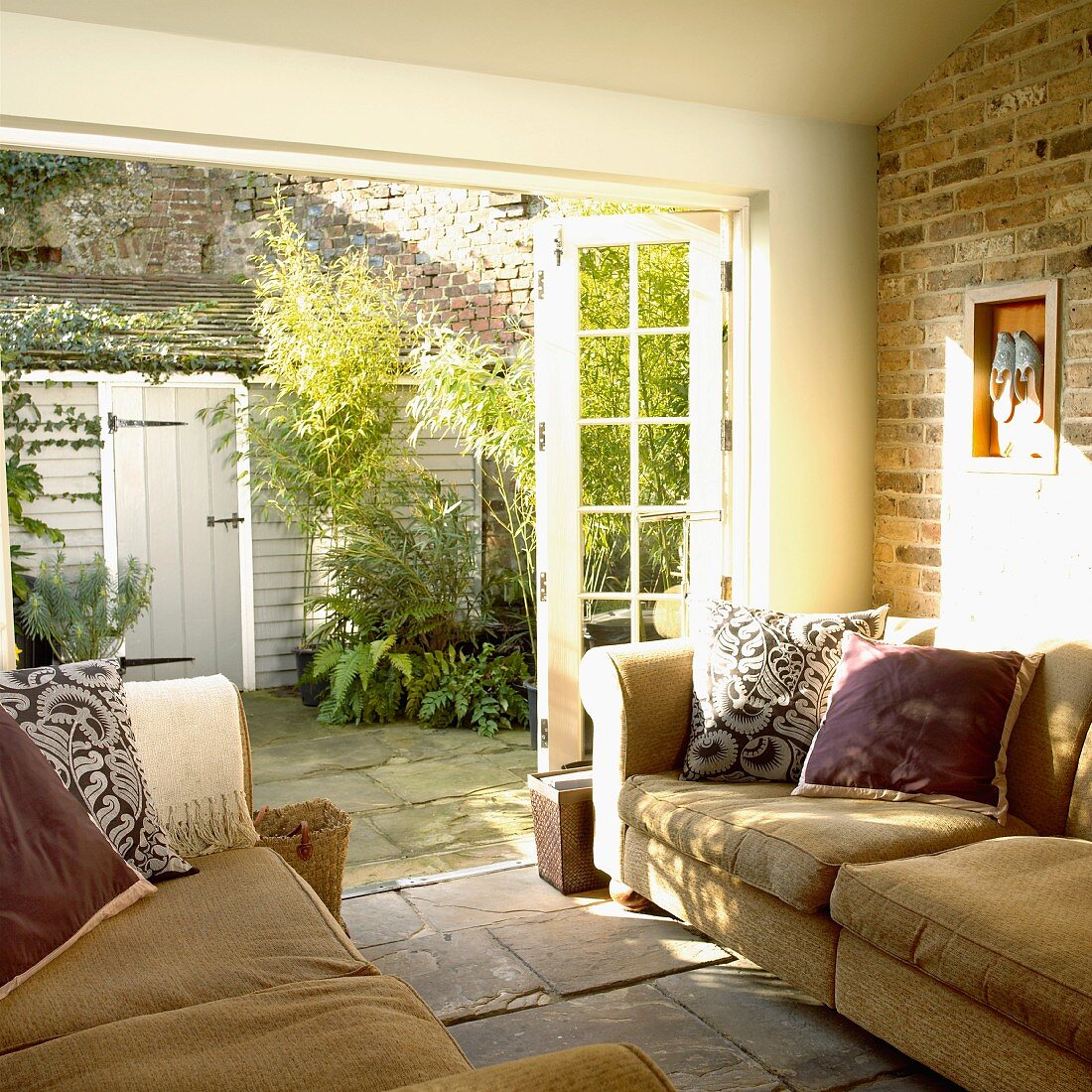 Living room with sectional sofas and open doors into a courtyard filled with green plants