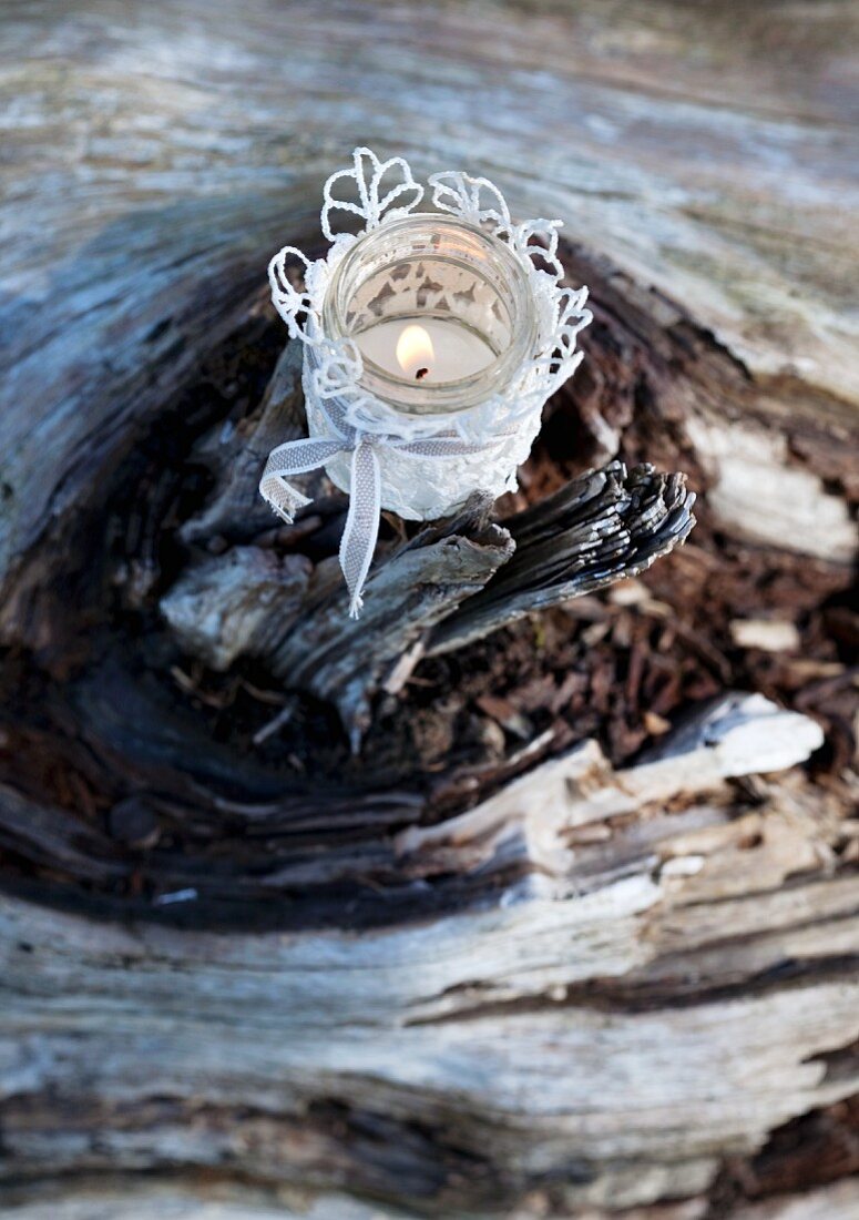 Romantic candle lantern made from glass jar with lace cover on weathered tree stump